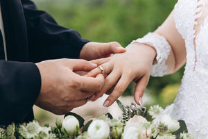 A newlywed husband puts a wedding ring on his bride’s finger, who’s wearing 2027 wedding dress trends.