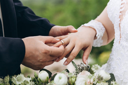 A newlywed husband puts a wedding ring on his bride’s finger, who’s wearing 2027 wedding dress trends.