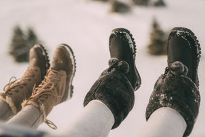 Two sets of feet in the snow showing fur boots outfit options.
