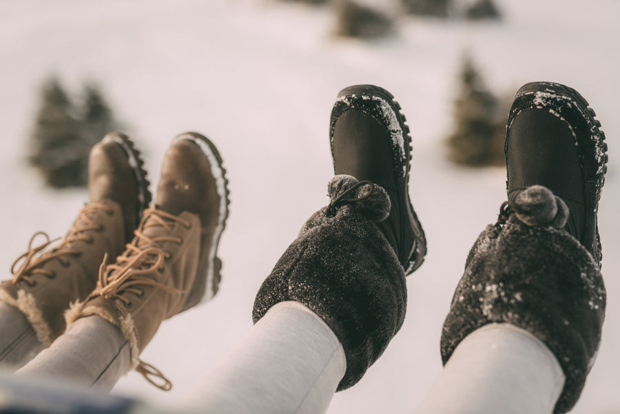 Two sets of feet in the snow showing fur boots outfit options.