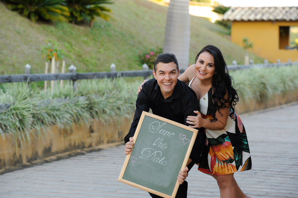 portrait of beautiful young wedding couple posing at outdoor photo shoot holding Save the date sign. Engagement Photo Outfit Ideas