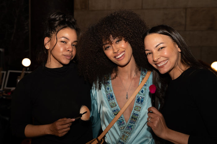 A model in a blue satin robe with the hair and makeup team backstage