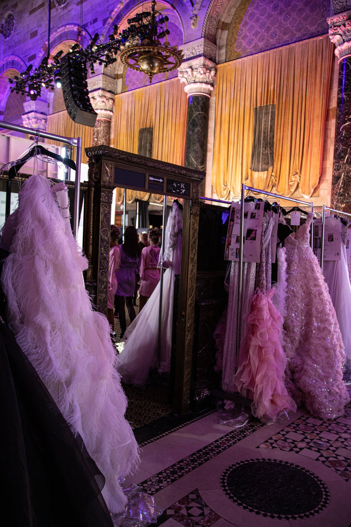 The bridal gowns and the pink feathered ballgown on the rack backstage