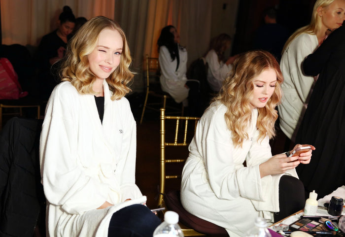 Models in white robes in hair and makeup backstage