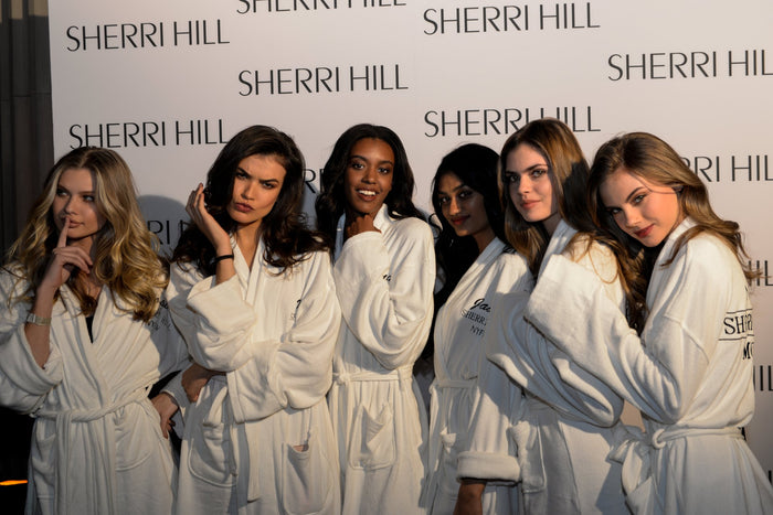 Sherri Hill with the models in white robes on the step-and-repeat