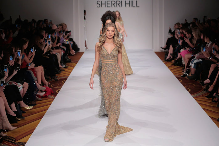 Model Josie Canseco in a gold beaded gown comes down the runway, seen from the front row