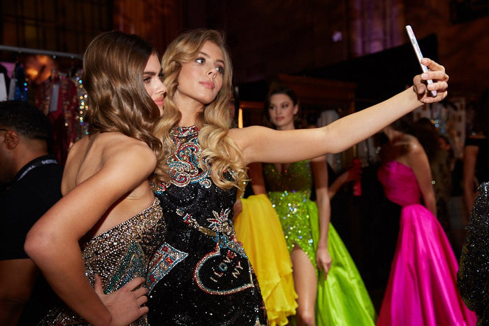 Models take a selfie backstage, with the lime and hot pink gowns behind them