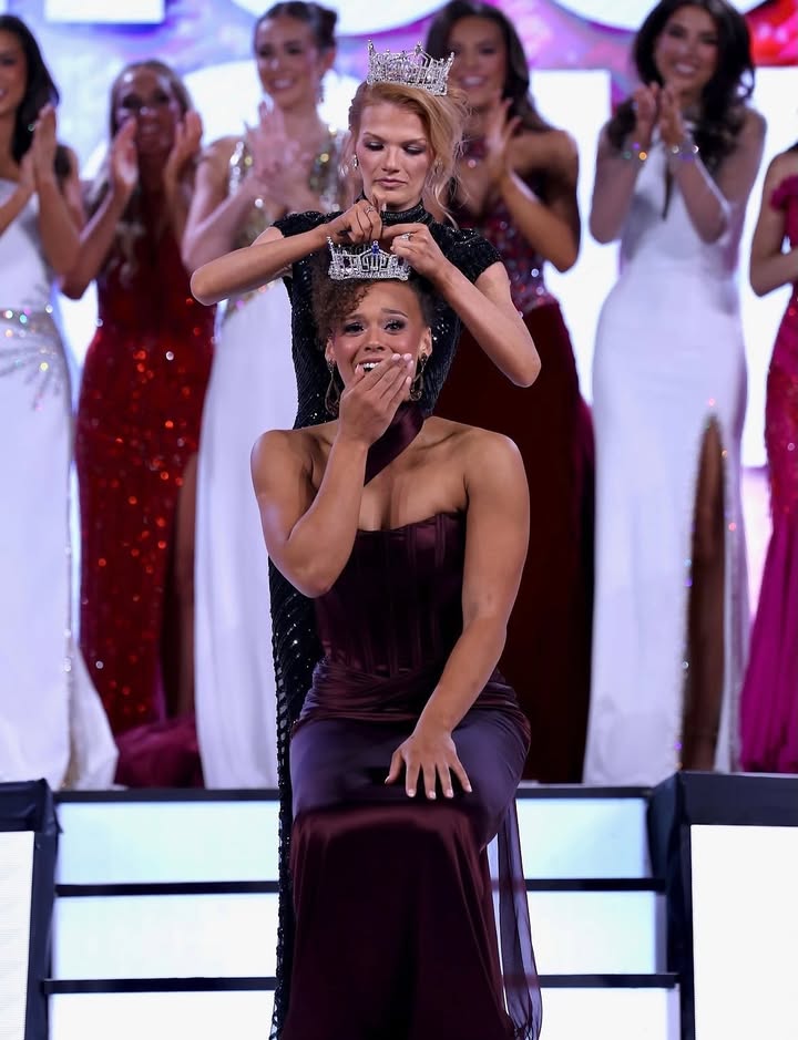 A new titleholder is crowned on stage as fellow contestants in evening gowns applaud