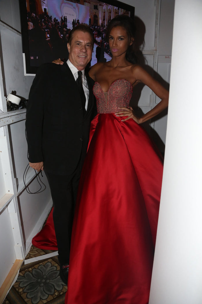 A model in a strapless red ball gown backstage before her walk