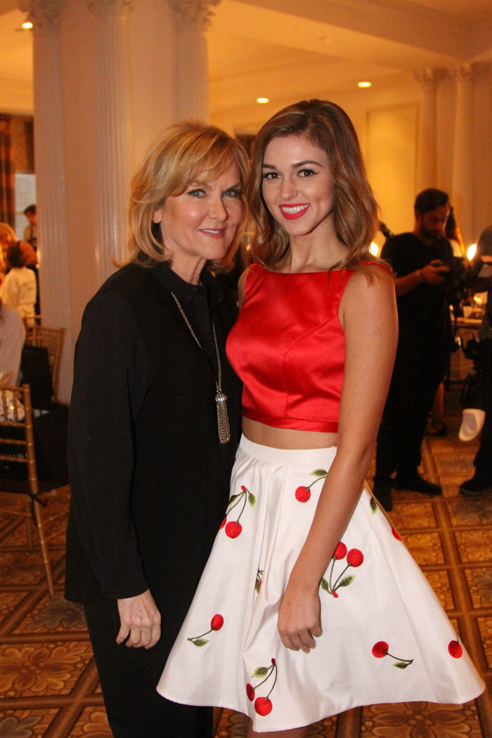 Sherri Hill with a guest in a red top and cherry-print skirt backstage