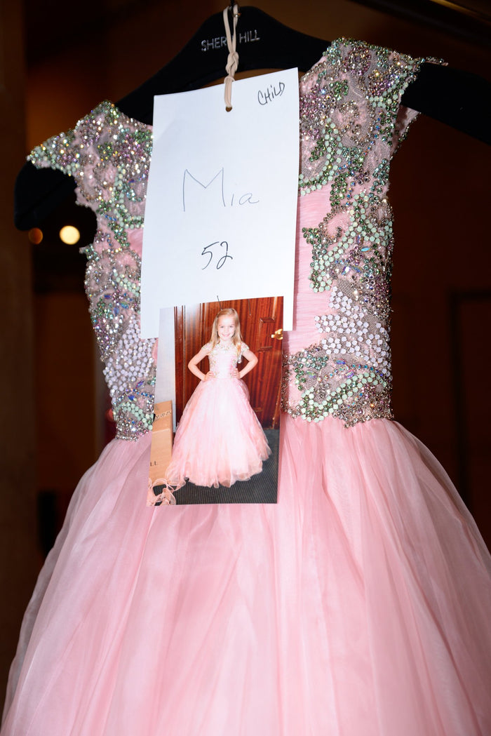 The pink cap-sleeve ballgown from look 52 on the rack backstage, with its look card