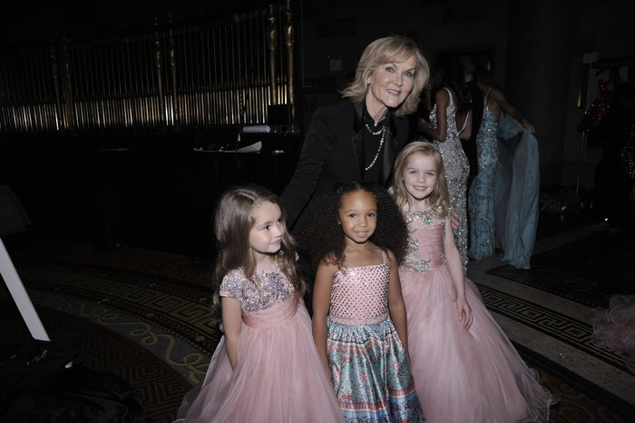 Sherri Hill with three young models in pink and print ballgowns before the show