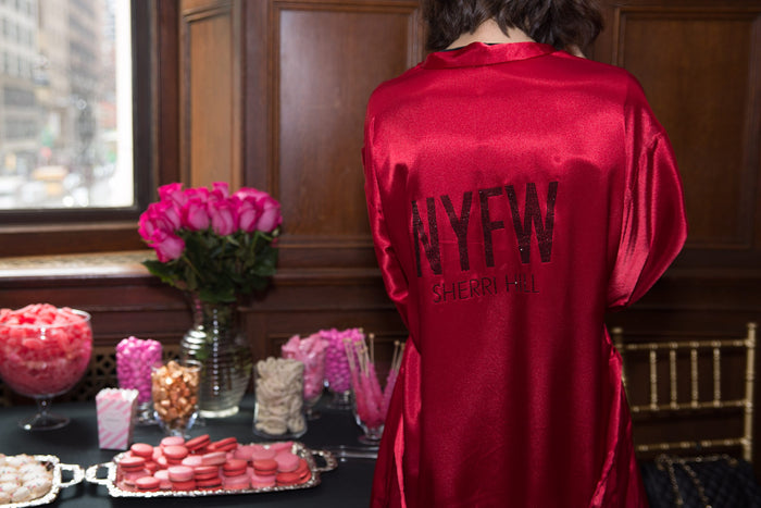A model in a red satin #NYFW robe at the flower and sweets table backstage