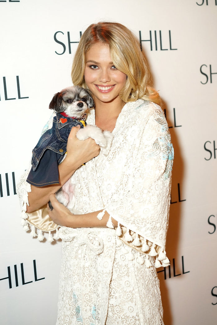 A model in a white Sherri Hill robe holds a small dog on the step-and-repeat
