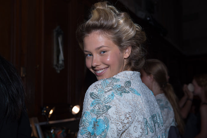 A model in a white embroidered Sherri Hill robe in hair and makeup