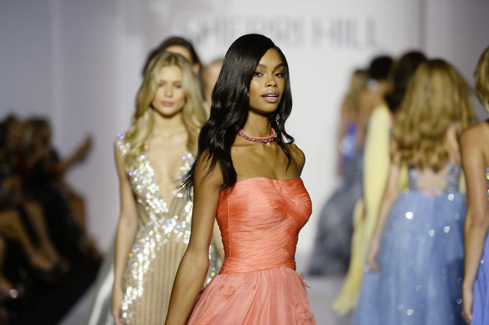 A coral chiffon gown passes the front row, with a sequin gown behind