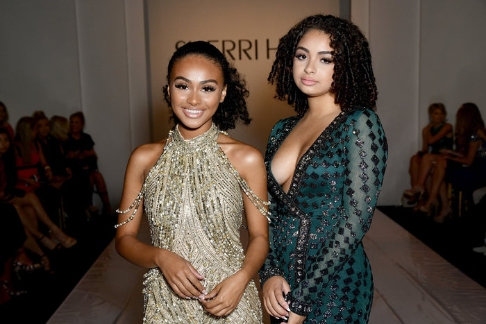 Two guests in gold and green beaded gowns in the front row before the show