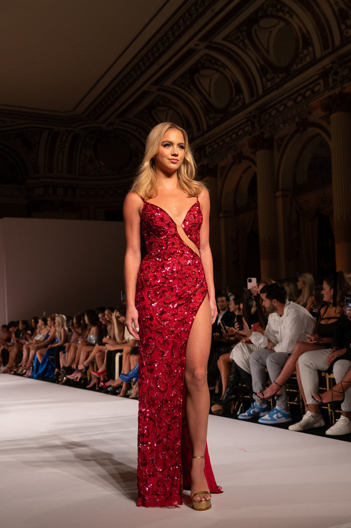Model Emma Brooks in a red beaded gown on the runway, seen from the front row