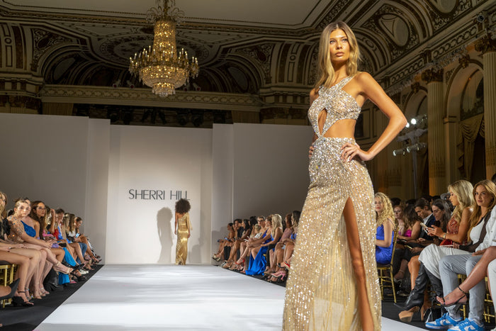 Model Fiona Briseno in a gold beaded gown on the runway under the chandeliers